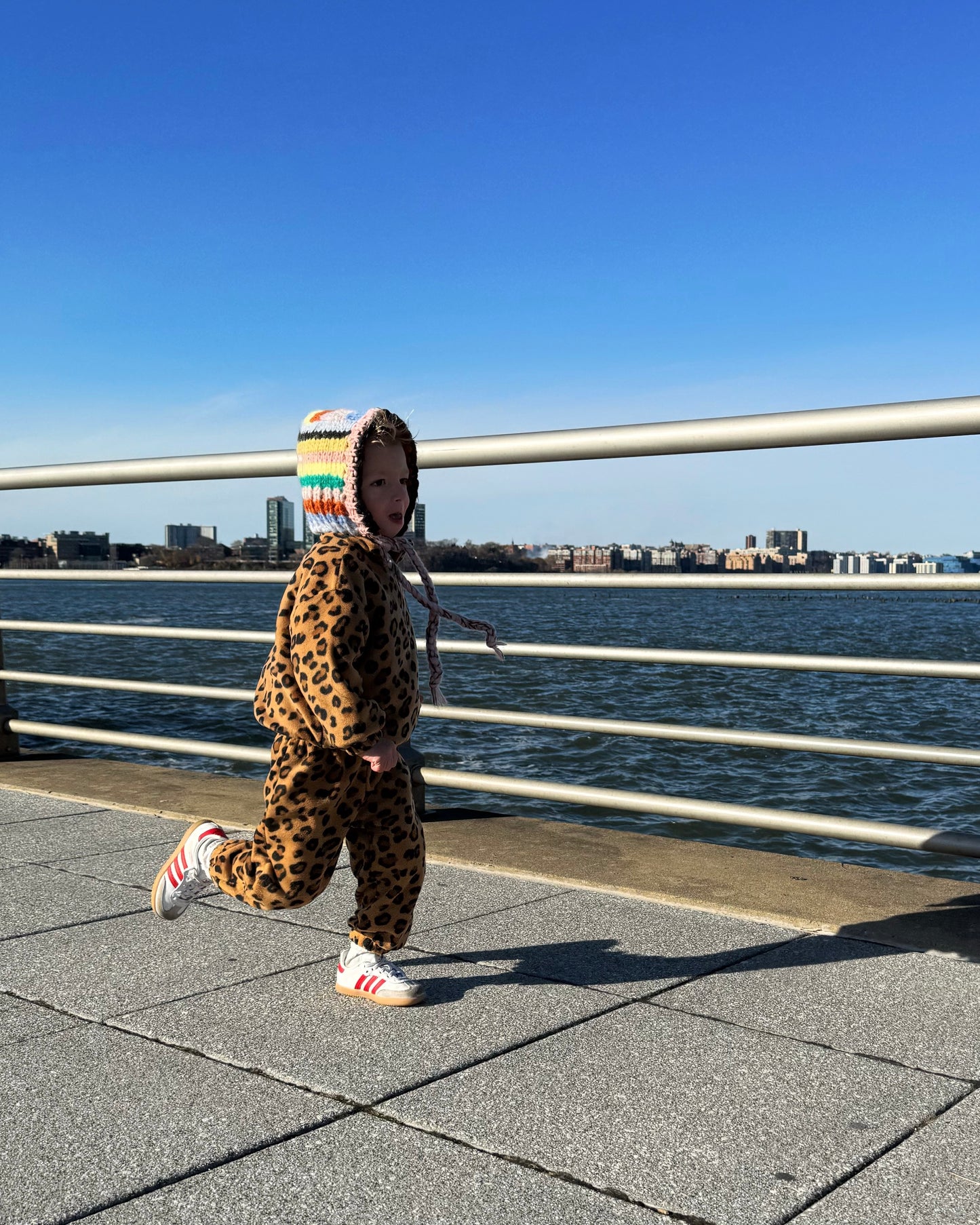 Child in leopard print outfit running at a waterfront park in NYC.