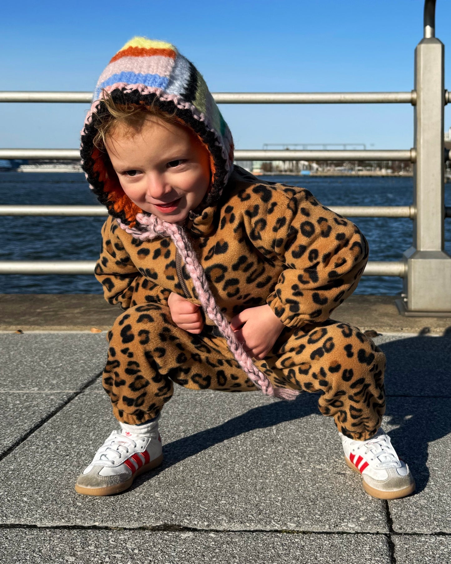 Child in leopard print outfit with colorful hood by a waterfront