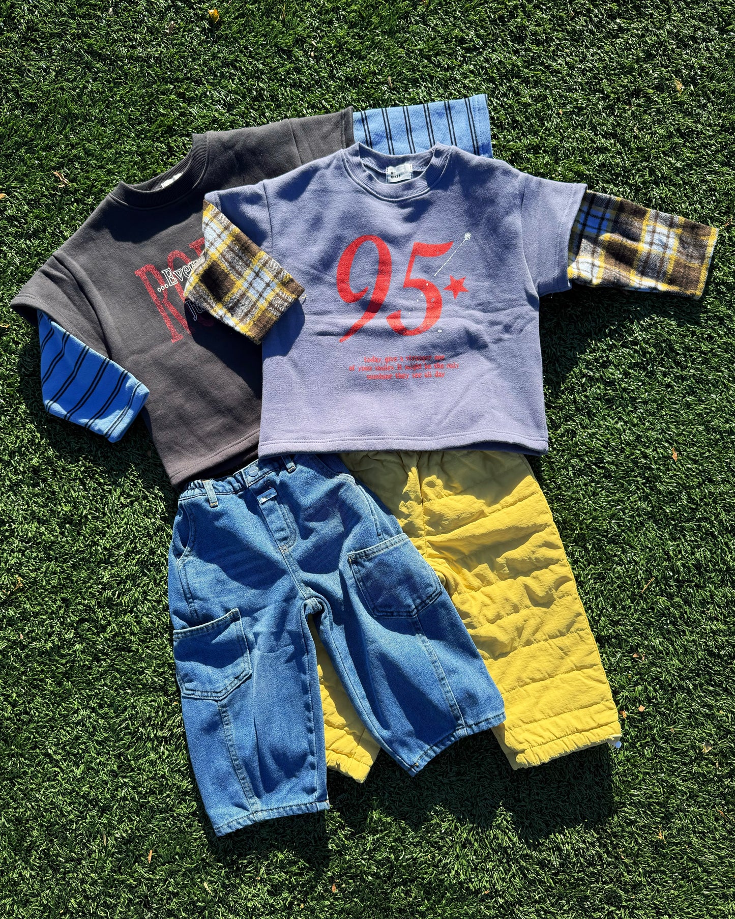 Cozy children's clothing including layered shirts, jeans, and a padded winter pants on grass