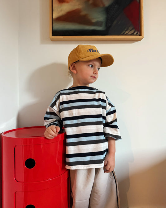 Child wearing a striped shirt and yellow cap standing next to red Kartell drawers indoors.