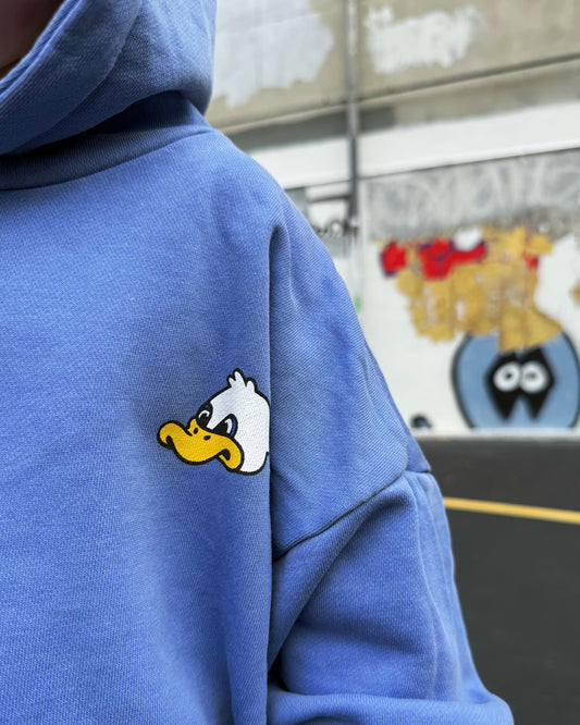 Blue hoodie with a duck cartoon character face patch on the sleeve, blurred background