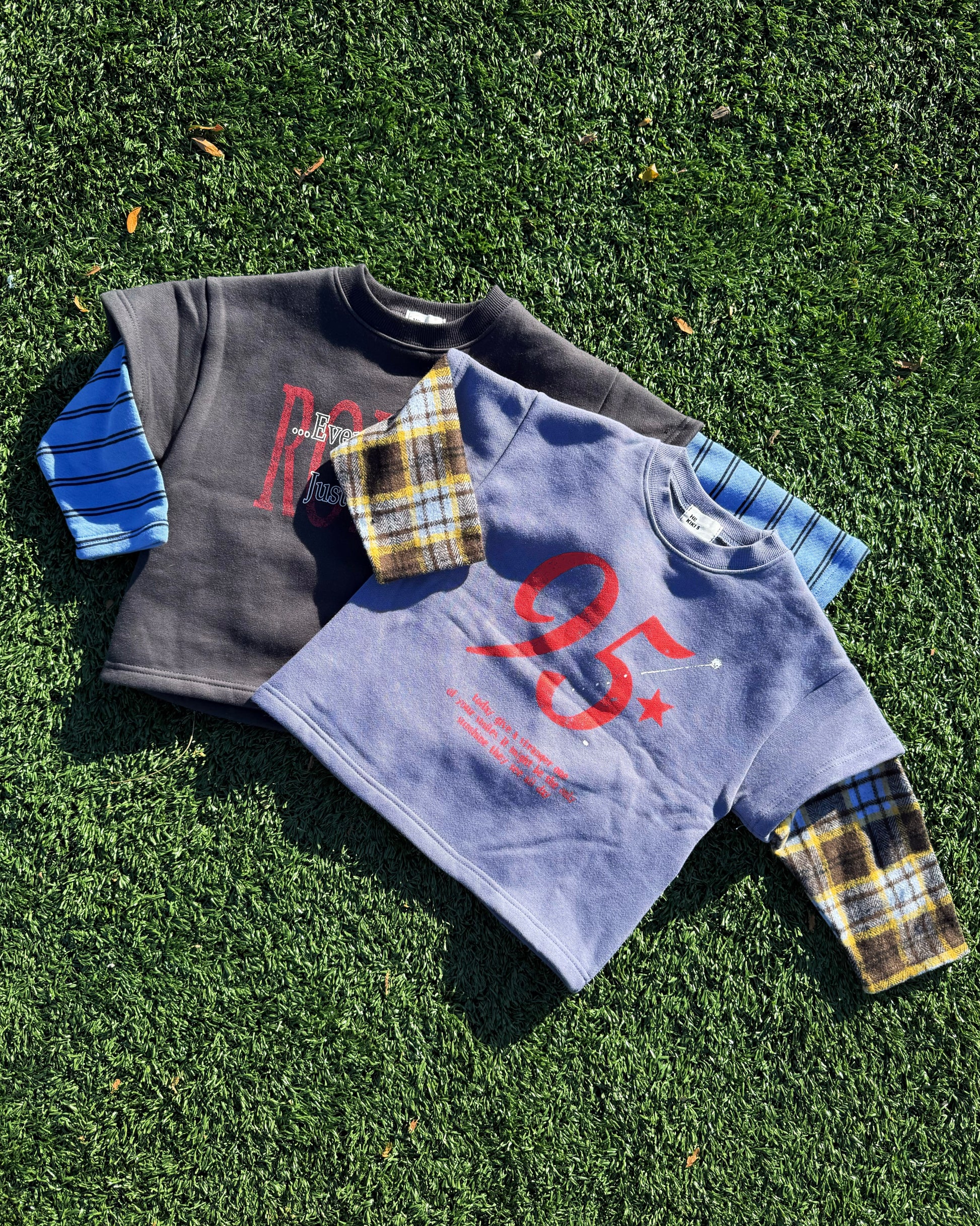 Two children's sweatshirts with plaid sleeves on a grassy surface