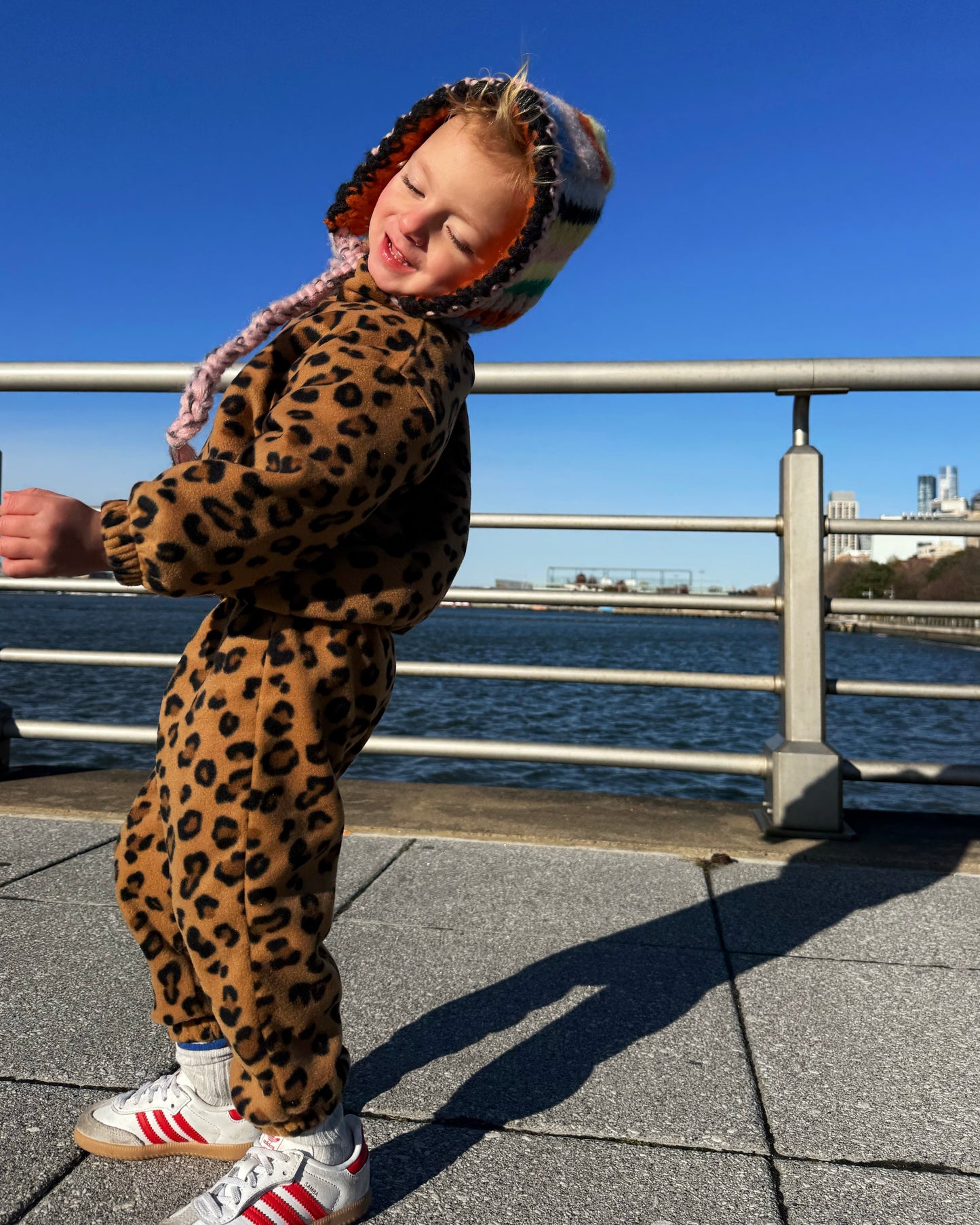 Child wearing a leopard print outfit with a hood by a waterfront on a clear day