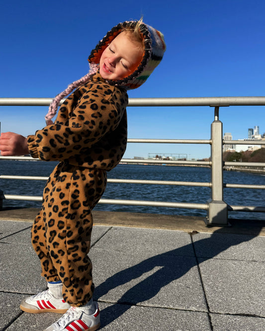 Child wearing a leopard print outfit with a hood by a waterfront on a clear day