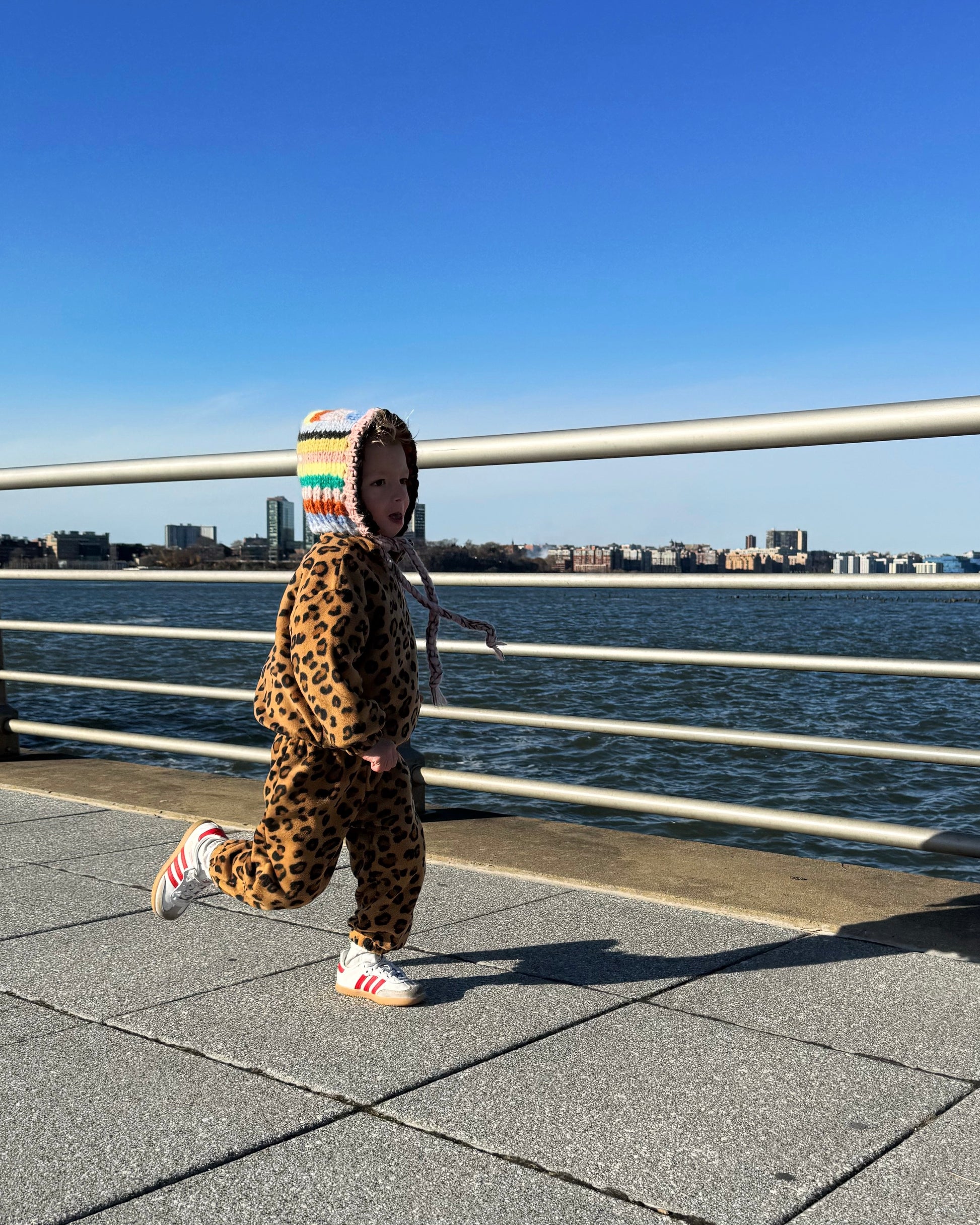 Child in leopard print outfit running at a waterfront park in NYC. 