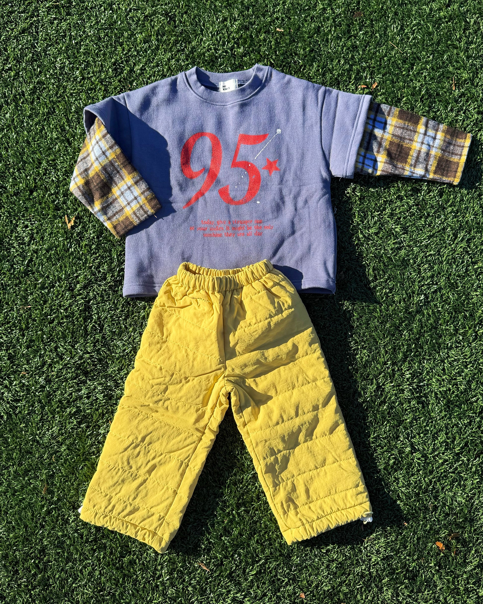 Children's outfit with a blue shirt featuring the number 95 and cozy yellow pants on grass.