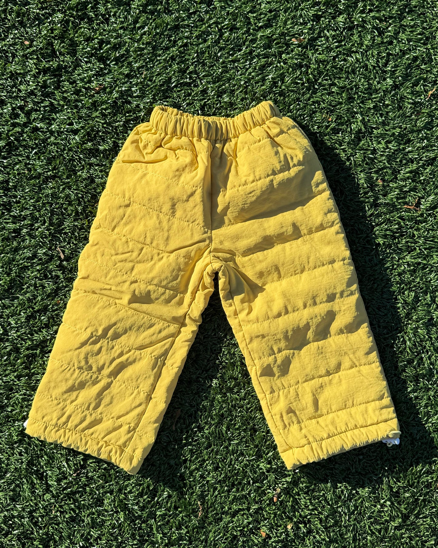 Kids yellow padded winter pants on a grassy surface