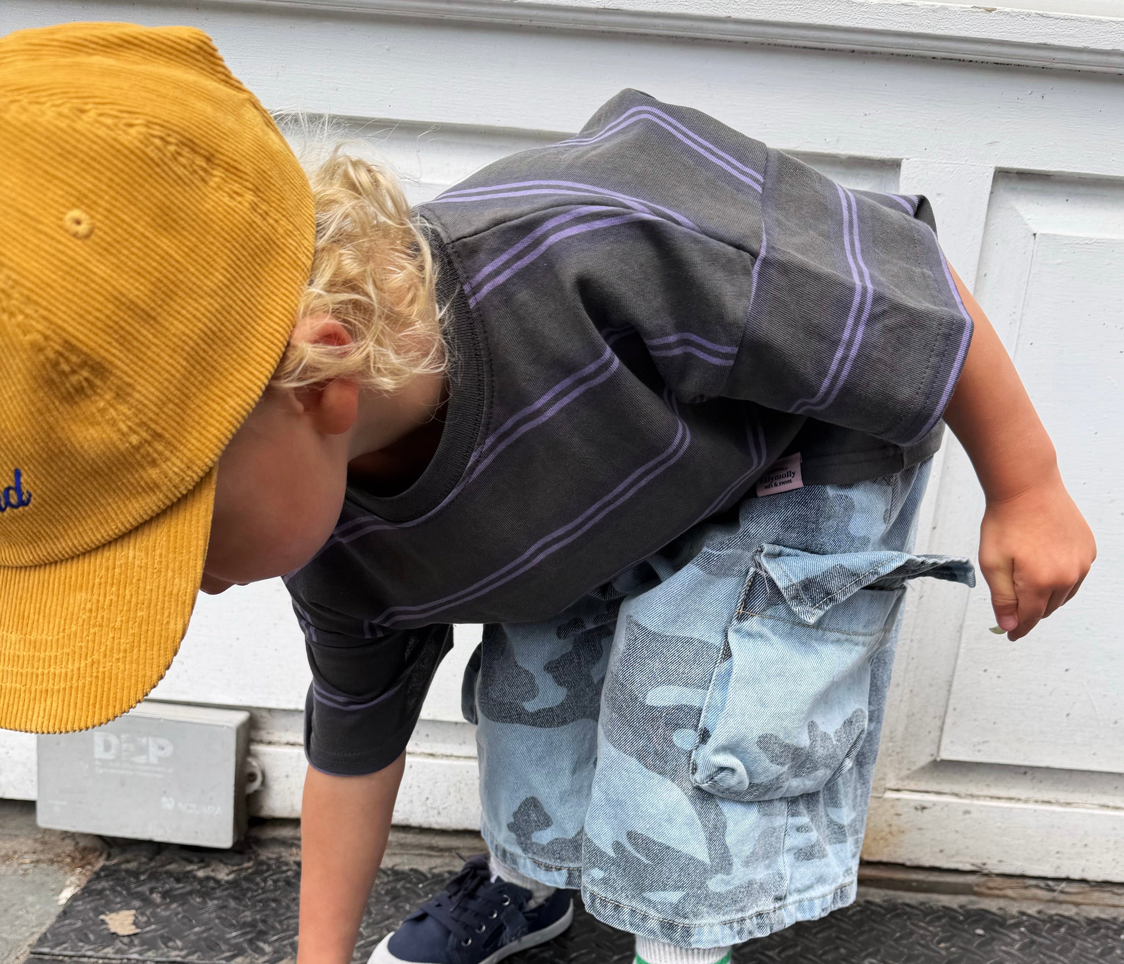 Two children playing on a street, one wearing a yellow cap and the other in a gray outfit with blue shoes.