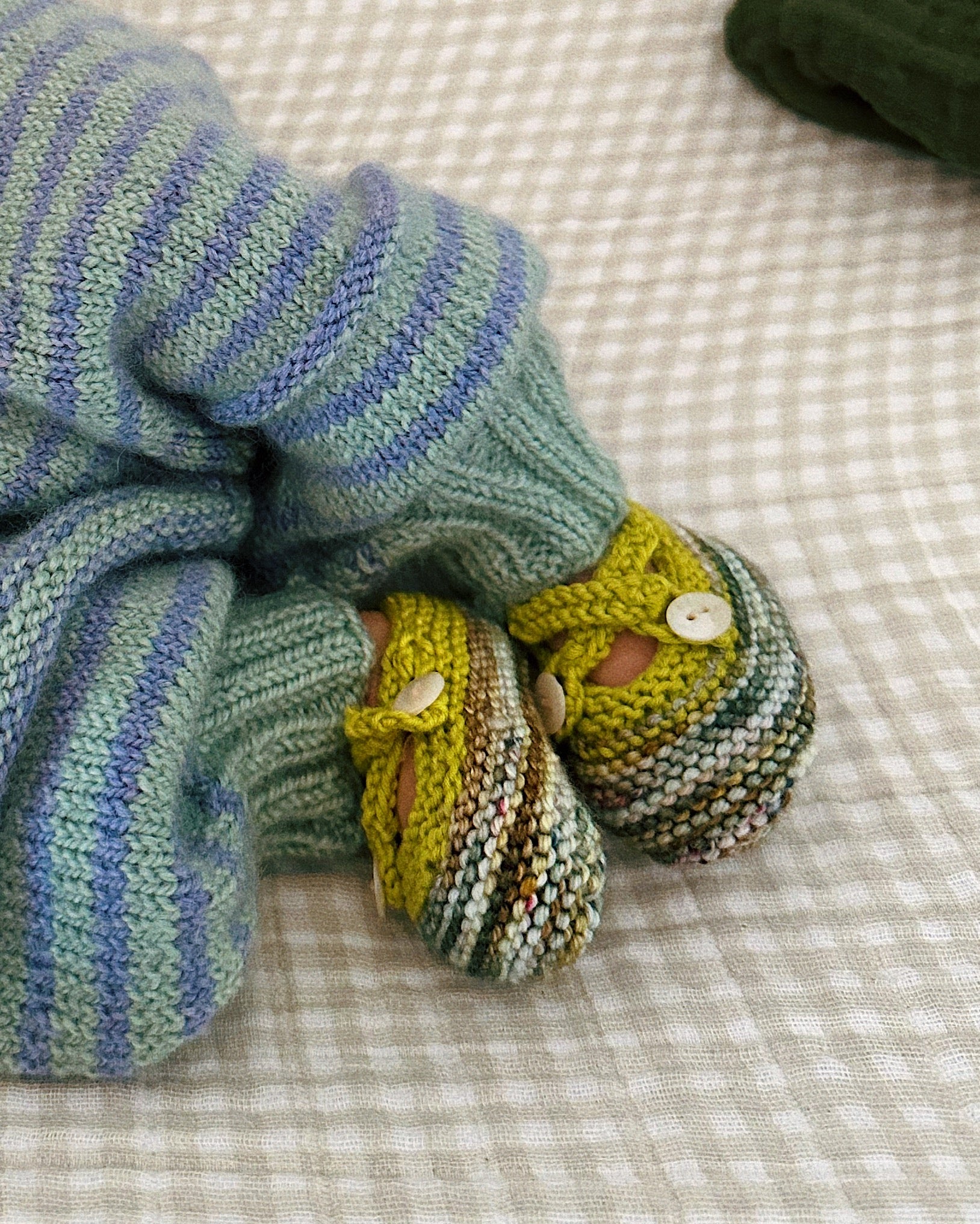 Knitted baby booties with a blanket on a checkered fabric background